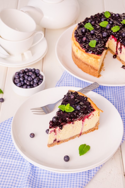 Cheesecake crème délicieux avec zeste de citron et confiture de myrtilles sur une plaque sur un fond en bois blanc