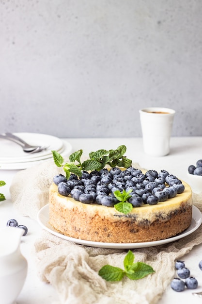 Cheesecake à la new yorkaise, myrtilles fraîches et menthe sur une assiette blanche.