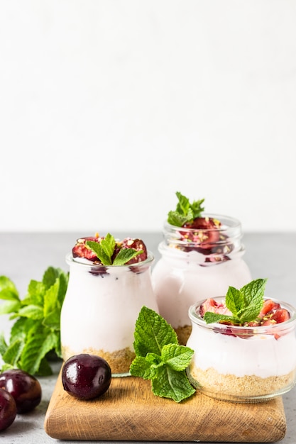 Cheesecake non cuit au four avec des cerises dans des bocaux en verre, des cerises fraîches et de la menthe. Dessert sain.