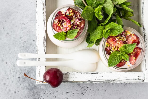 Photo cheesecake non cuit au four avec des cerises dans des bocaux en verre, des cerises fraîches et de la menthe. dessert sain.