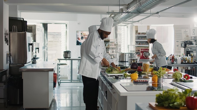 Chef afro-américain coupant du céleri frais sur une planche à découper, préparant des ingrédients pour un repas gastronomique et une recette culinaire. Cuisinier masculin utilisant des ustensiles professionnels pour préparer un plat gastronomique.