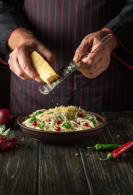 Le chef ajoute du fromage sur des spaghettis aux légumes dans une assiette