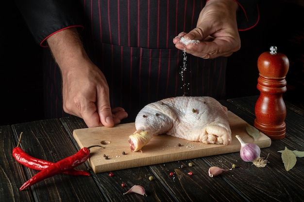 Le chef ajoute du sel à la cuisse de poulet dans la cuisine Concept de recette de cuisine délicieuse pour l'hôtel