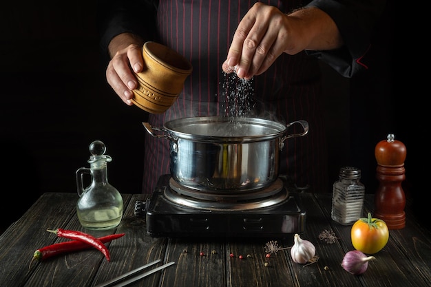 Le chef ajoute du sel à la marmite de plats chauds Cuisiner un déjeuner diététique dans la cuisine de l'hôtel ou du restaurant