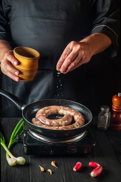 Le chef ajoute du sel à la poêle avec des saucisses de viande crue