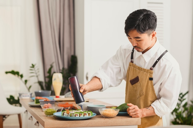 Un chef asiatique qui prépare des rouleaux de sushi dans la cuisine ajoute de la sauce au concept de livraison de sushis