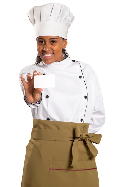 Chef, boulanger ou cuisinier femme montrant une carte vierge portant l'uniforme et un chapeau de chefs. Carte vierge pour menu, carte-cadeau, offre, etc. Belle femme africaine / noire isolée sur espace blanc