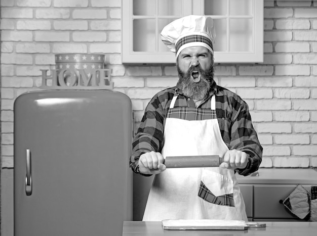 Chef boulangers en colère homme soulevant un rouleau à pâtisserie menaçant dans la cuisine blanche