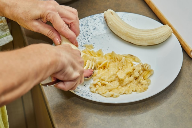 Le chef broie la banane avec une fourchette pour faire de la tarte dans la cuisine de la maison.