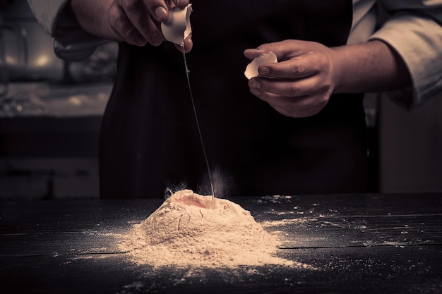 Le chef casse les œufs en farine sur une table en bois