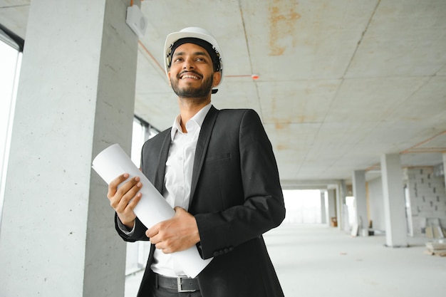 Chef de chantier indien debout portant un casque pensant au chantier de construction Portrait d'un travailleur manuel ou d'un architecte de race mixte