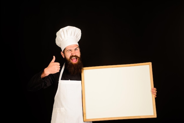 Le chef clignotant tient le tableau noir montre le pouce vers le haut homme cuisinier montre le tableau de menu vide avec espace de copie