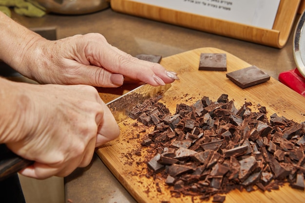 Le chef coupe le chocolat amer en morceaux sur une planche de bois dans la cuisine