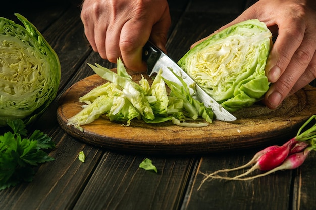 Le chef coupe le chou frais avec un couteau sur une planche à découper avant de préparer un plat végétarien