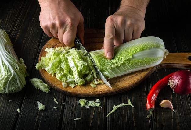 Le chef coupe du chou napa frais avec un couteau pour la salade sur une planche de cuisine vintage avec des légumes frais Concept de cuisine et de restaurant ou de café