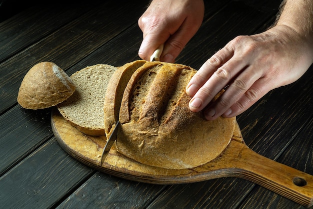 Le chef coupe du pain de blé avec un couteau sur une planche à découper en bois Pain de blé sur la table de la cuisine ou le concept d'alimentation saine et de boulangerie traditionnelle