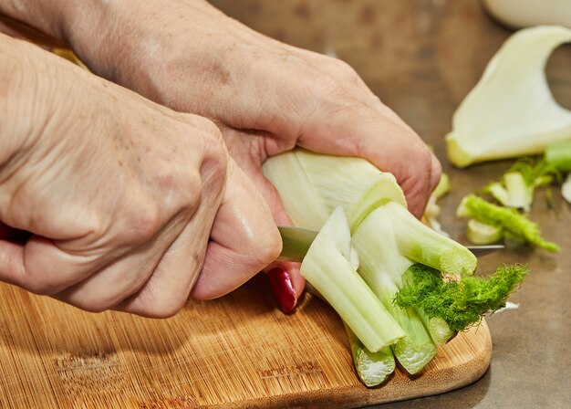 Le chef coupe le fenouil selon la recette de cuisine sur planche de bois dans la cuisine