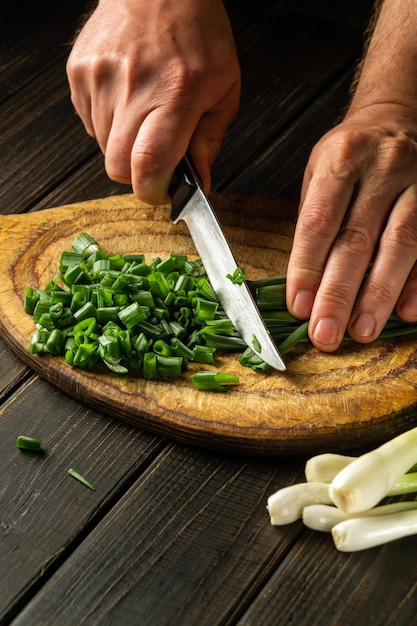 Le chef coupe des feuilles d'oignon vert sur une planche à découper vintage avant de préparer un délicieux plat