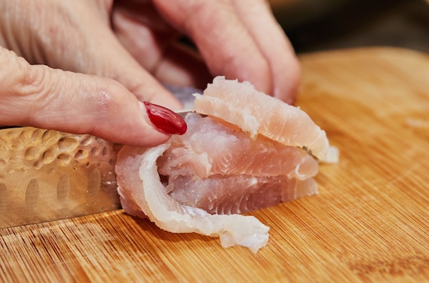 Le chef coupe les filets de poisson sur planche de bois pour la cuisson.