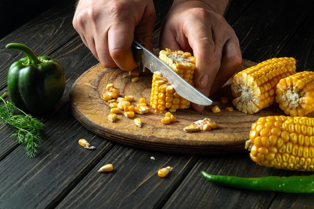 Photo le chef coupe le maïs avec un couteau le maïs est un excellent petit-déjeuner ou déjeuner diététique préparé par les mains du cuisinier