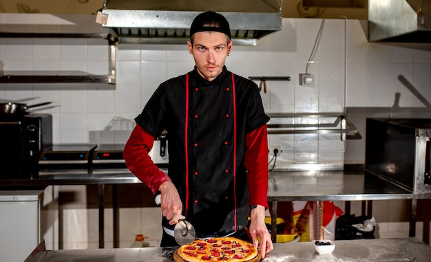 Le chef coupe la pizza avec un couteau pour servir