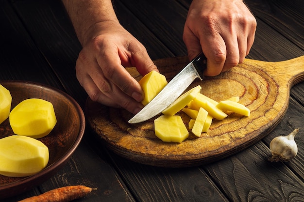 Le chef coupe des pommes de terre épluchées avec un couteau sur une planche à découper