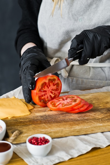 Chef coupe les tomates rouges. Le concept de la cuisson d&#39;un burger noir.