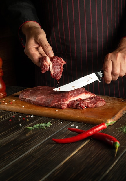 Le chef coupe la viande de boeuf fraîche crue sur une planche à découper avant la cuisson ou le barbecue