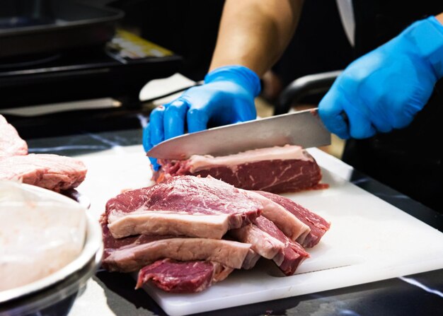 Le chef coupe de la viande crue avec un couteau sur une planche.