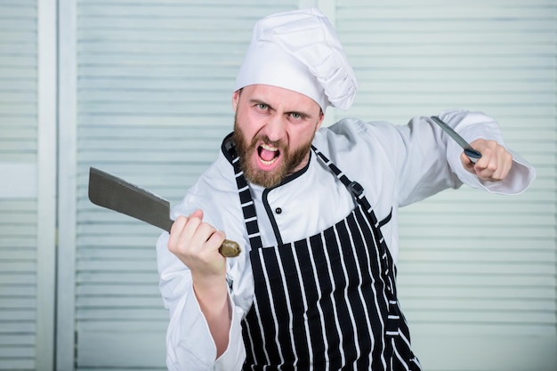 Photo chef avec des couteaux professionnel dans la cuisine cuisine culinaire homme barbu en colère avec un couteau aime manger de la nourriture homme confiant en tablier et chapeau cuisinier en uniforme de restaurant chef prêt pour la cuisson