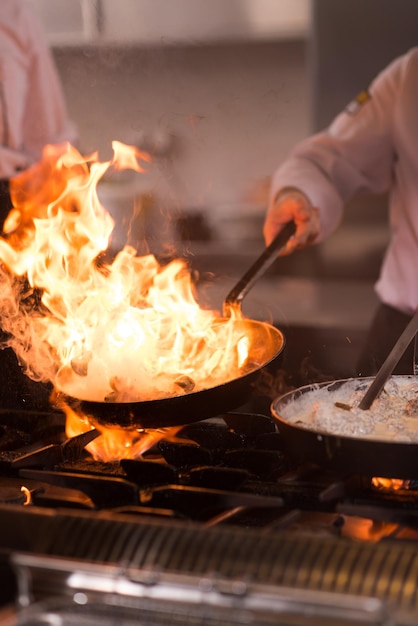 Chef cuisinant et faisant flamber sur la nourriture dans la cuisine du restaurant
