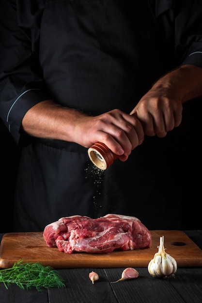 Chef cuisinant un filet de viande crue et ajoutant du poivre ou du piment pour la marinade sur fond noir