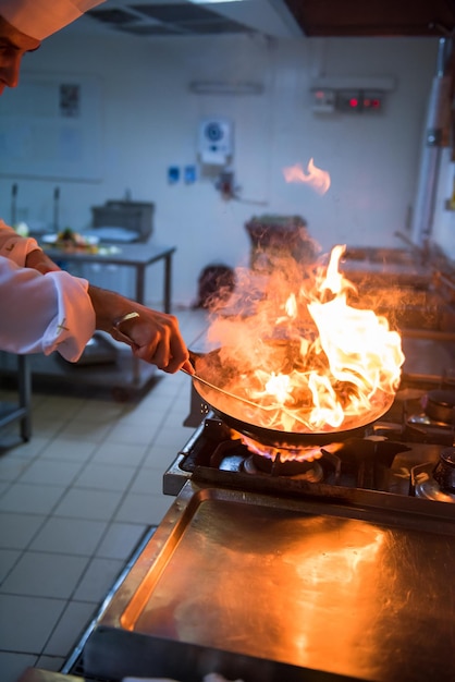 Chef cuisinant et flambant sur la nourriture dans la cuisine du restaurant