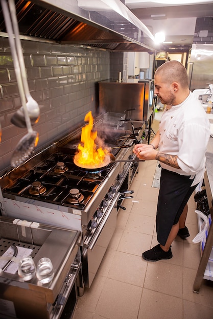 Chef cuisinant avec flamme sur sa cuisine de restaurant. Cuisinier qualifié