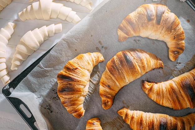 Le chef cuisine des croissants dans la cuisine le matin sur la table des croissants prêts à l'emploi et crus et les mêmes ingrédients pour leur préparation