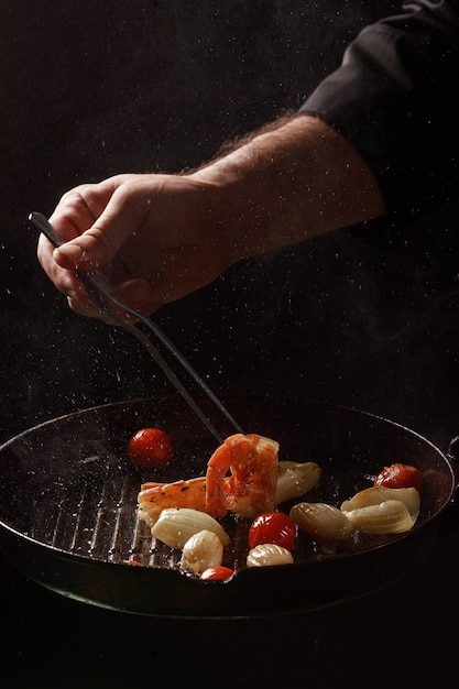 Le chef cuisine les fruits de mer, les crevettes dans une poêle avec des légumes