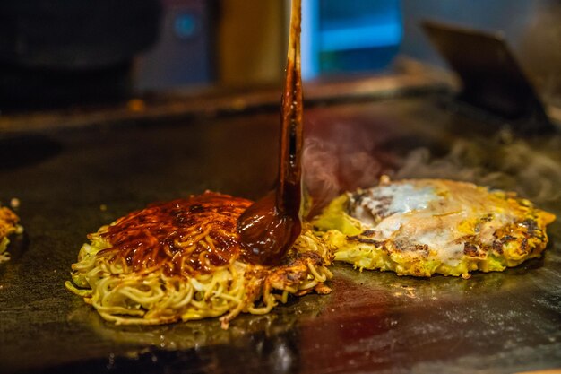 le chef cuisine des plats traditionnels japonais appelés Okonomiyaki, il ajoute de la sauce épicée dans la nourriture