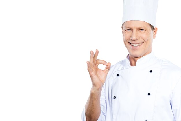 Chef cuisinier. Chef mûr confiant en uniforme blanc gesticulant signe OK et souriant en se tenant debout sur fond blanc