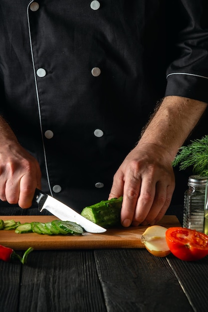 Chef ou cuisinier coupant un concombre vert dans la cuisine du restaurant. Faire une délicieuse salade avec des légumes frais