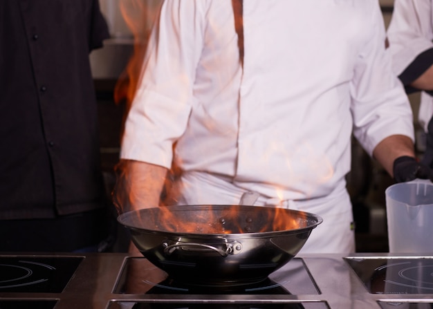 Chef cuisinier avec flamme dans une poêle sur une cuisinière