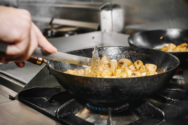 Chef de la cuisson des champignons dans une poêle sur feu brûlant