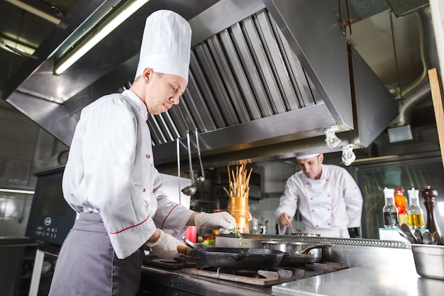 Chef dans la cuisine du restaurant au poêle avec poêle, cuisson