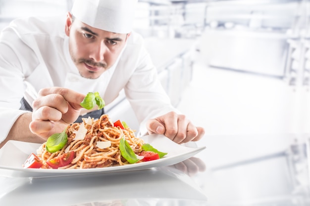 Le chef dans la cuisine du restaurant prépare et décore le repas avec les mains. Cuire la préparation de spaghettis bolognaise.