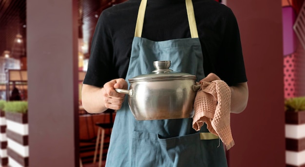 Un chef dans un plat de cuisine tablier tenant un pot dans la cuisine