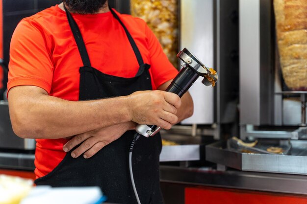 Chef du restaurant kebab utilisant l'outil électrique pour couper la viande de doner du grill