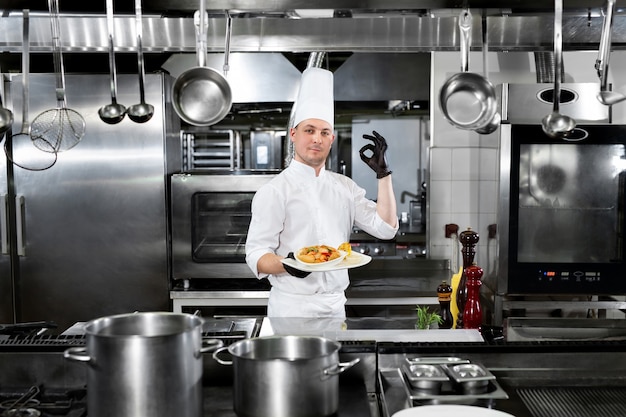 Le chef du restaurant tient une assiette avec un plat préparé et montre le signe "OK"