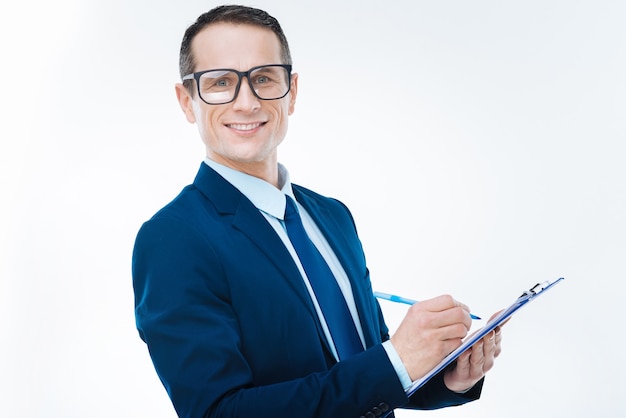 Chef d'entreprise. Heureux homme agréable et agréable souriant et prenant des notes tout en travaillant pour une société sérieuse