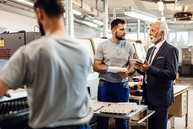 Chef d'entreprise mature communiquant avec un travailleur manuel lors de la visite d'une usine L'accent est mis sur le jeune homme