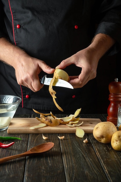 Le chef épluche les pommes de terre crues dans une cuisine d'hôtel avant de préparer un plat national