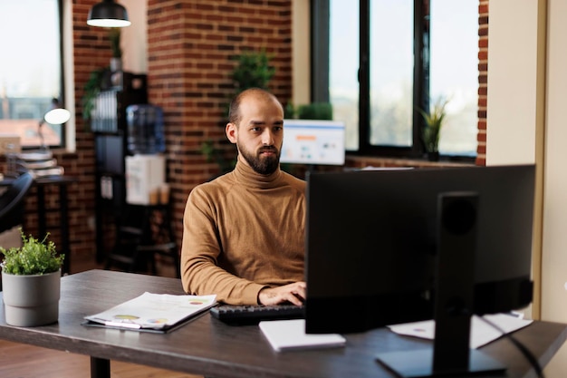 Chef d'équipe du département de recherche travaillant sur des solutions financières assis à son bureau et utilisant un ordinateur de travail. Chef de projet de démarrage analysant les résultats de la recherche et les données comptables.